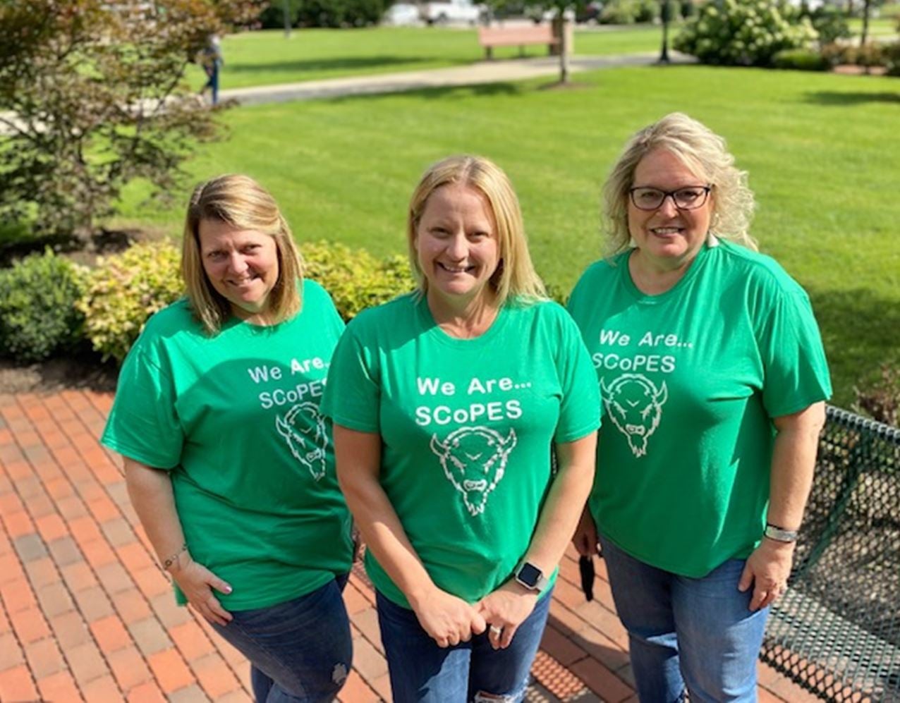 three people in green tshirts outside smiling at the camera