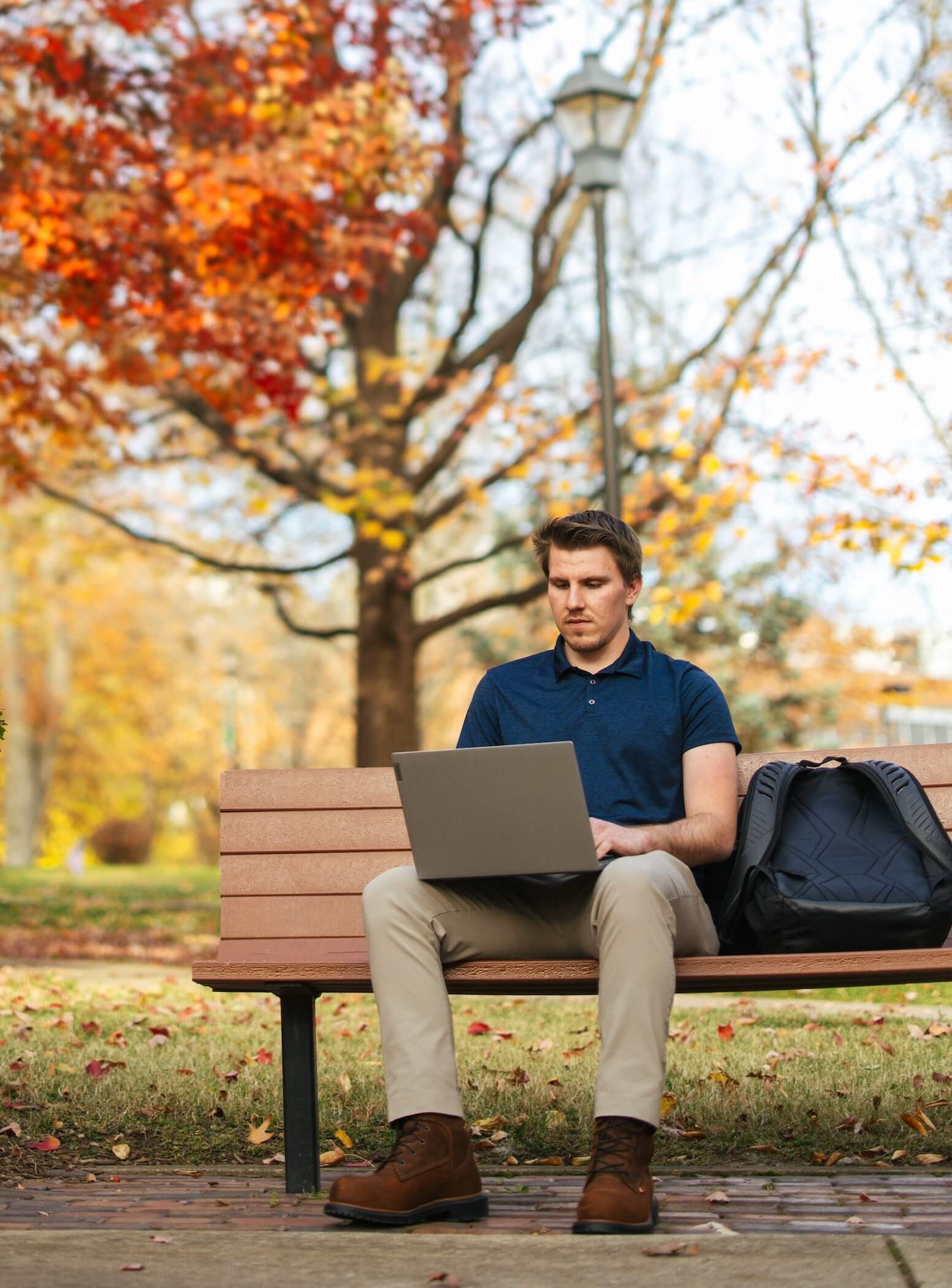 student sitting outside in the fall on a bench on a laptop