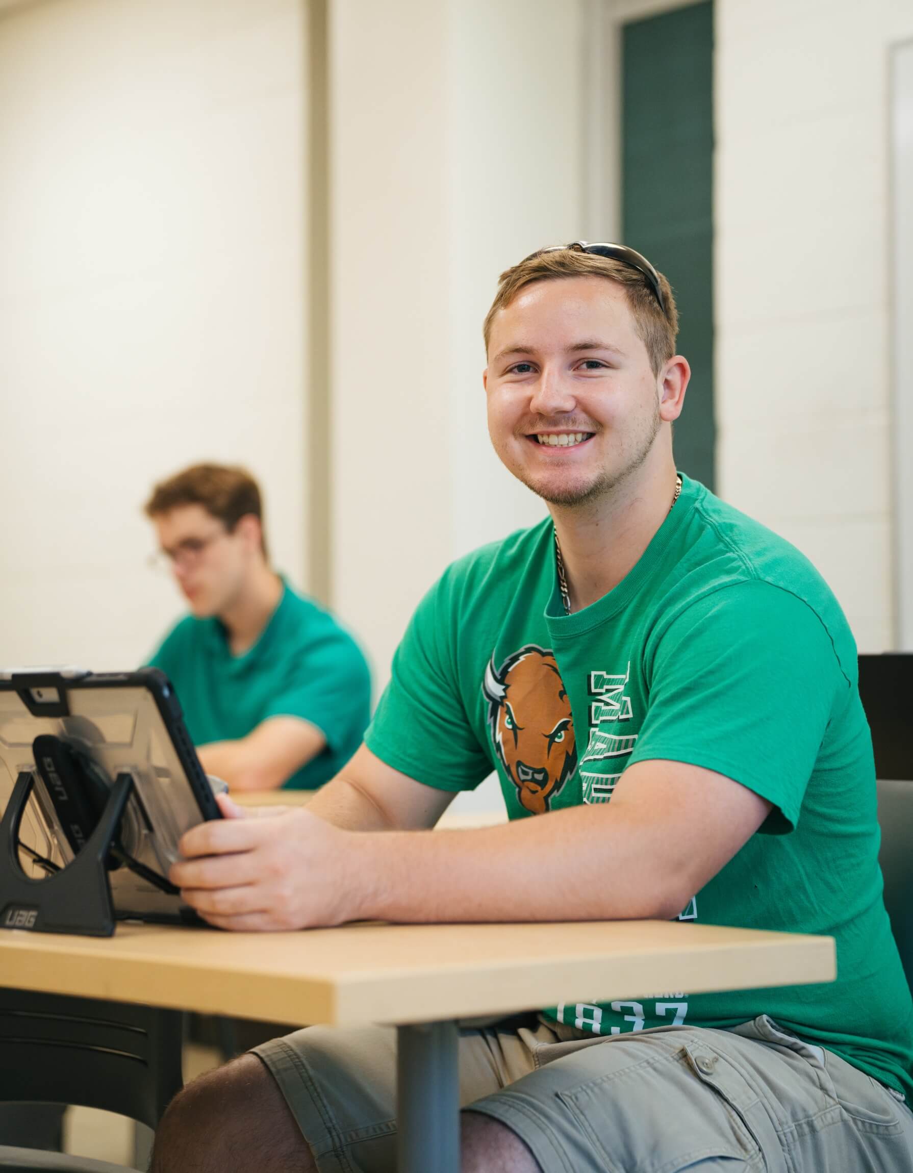 student working on an ipad at a desk and smiling at the camera