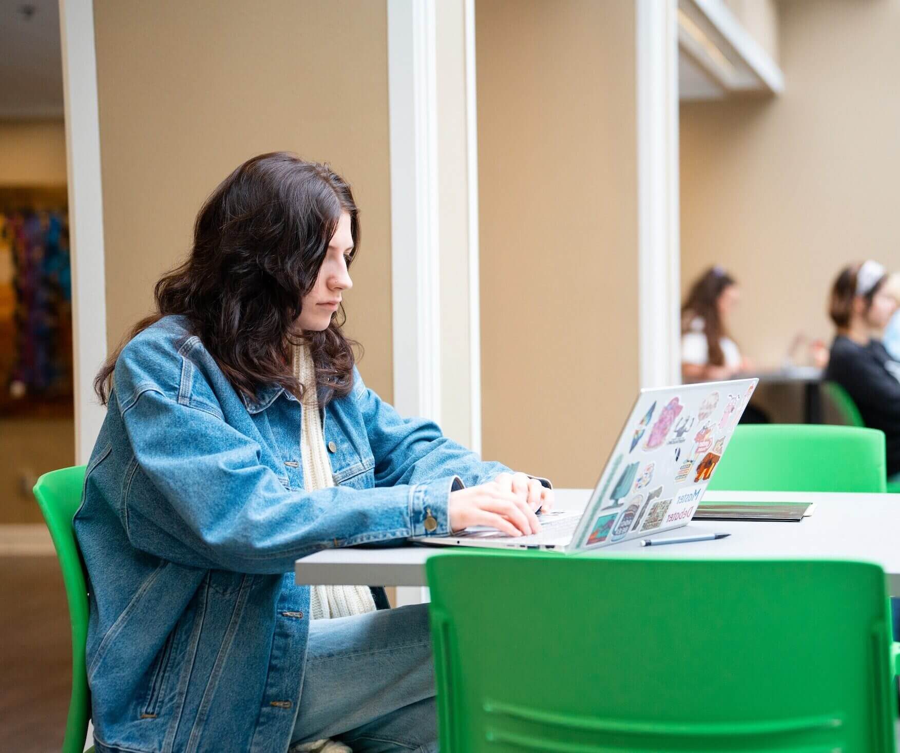 Student works on laptop in a building with other people around