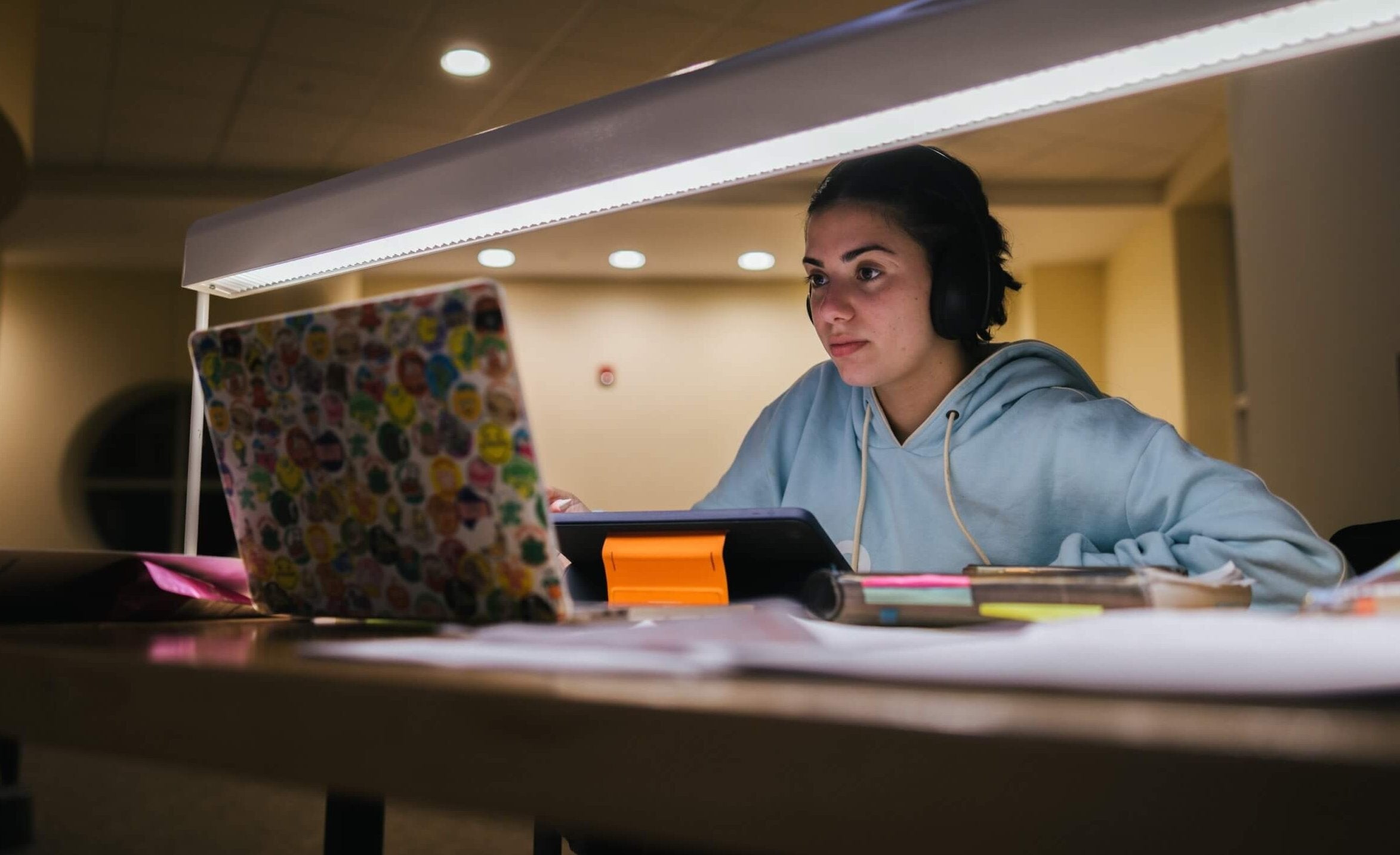 A student works on a laptop computer by the light of a desk lamp in a library