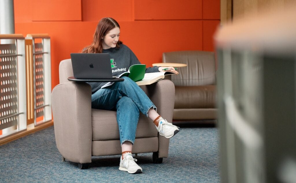 high school student working on a laptop and with a notebook in the library